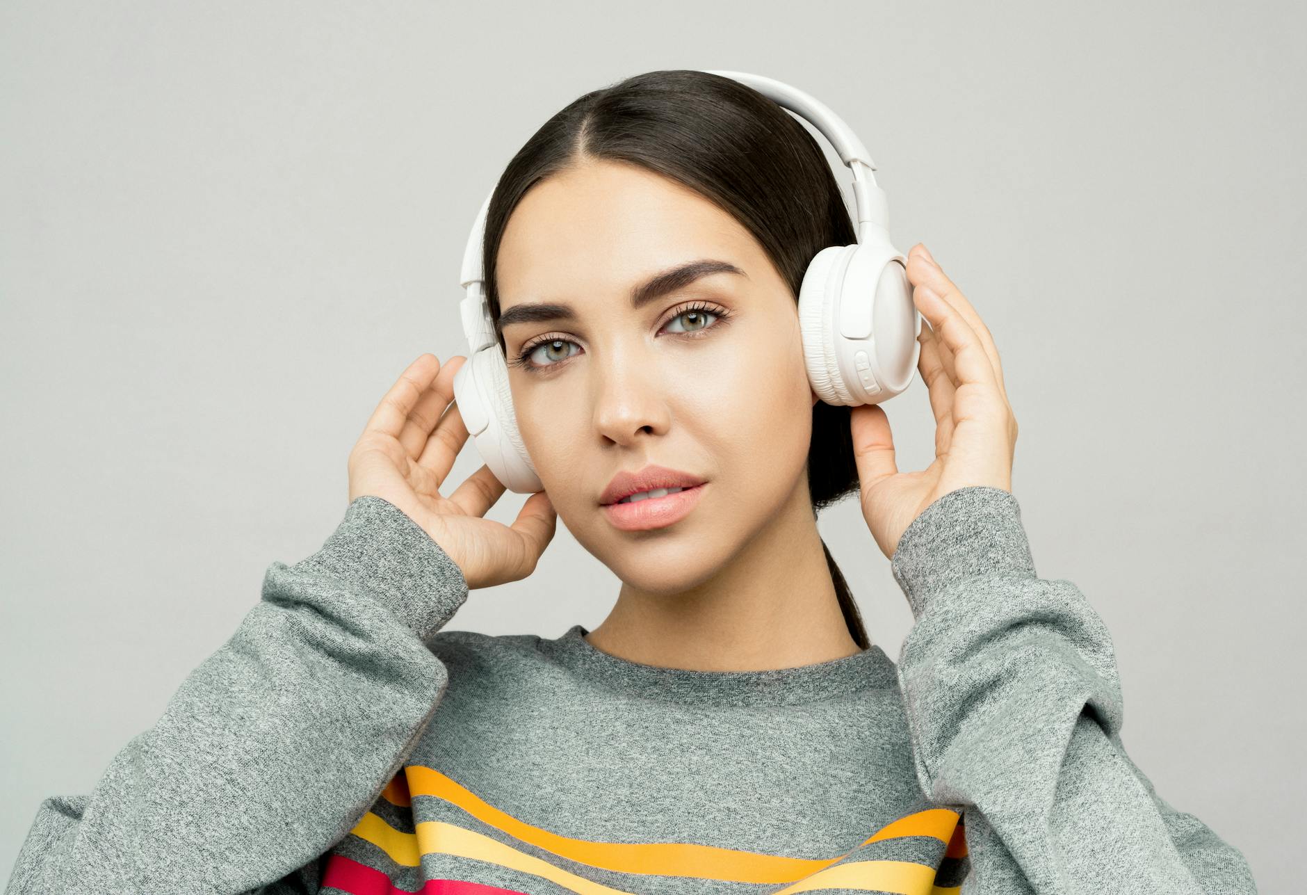 woman in gray and yellow sweater holding white headphones
