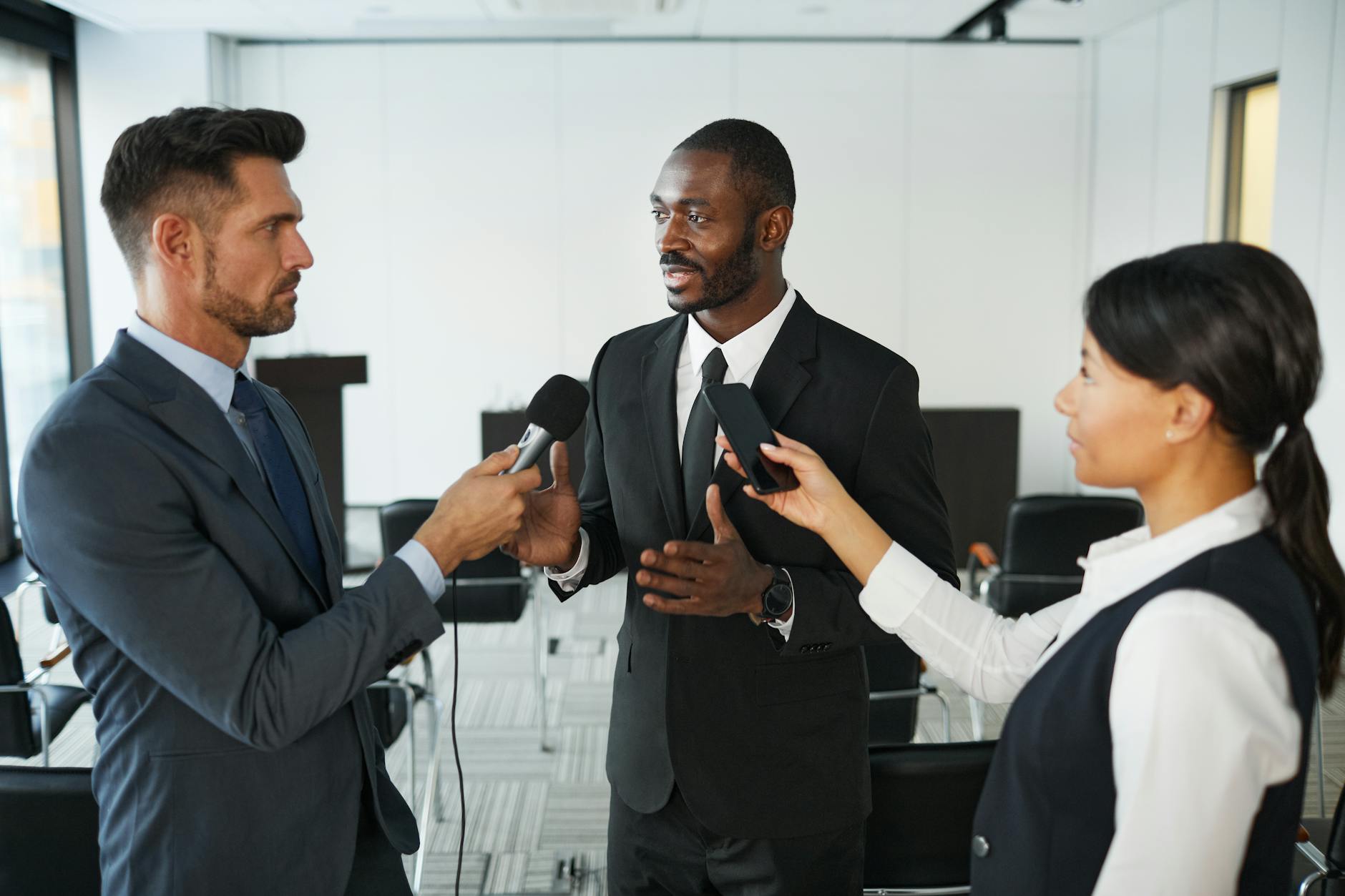 a man in black suit talking to a man and a woman