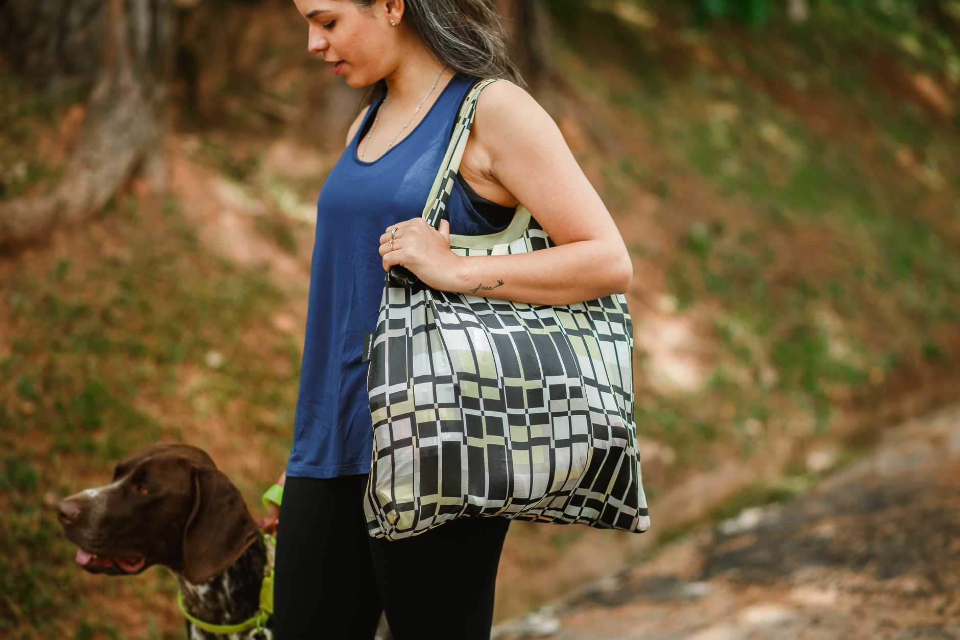 A woman walks her dog outside, carrying a trendy tote bag. Perfect blend of style and companionship.