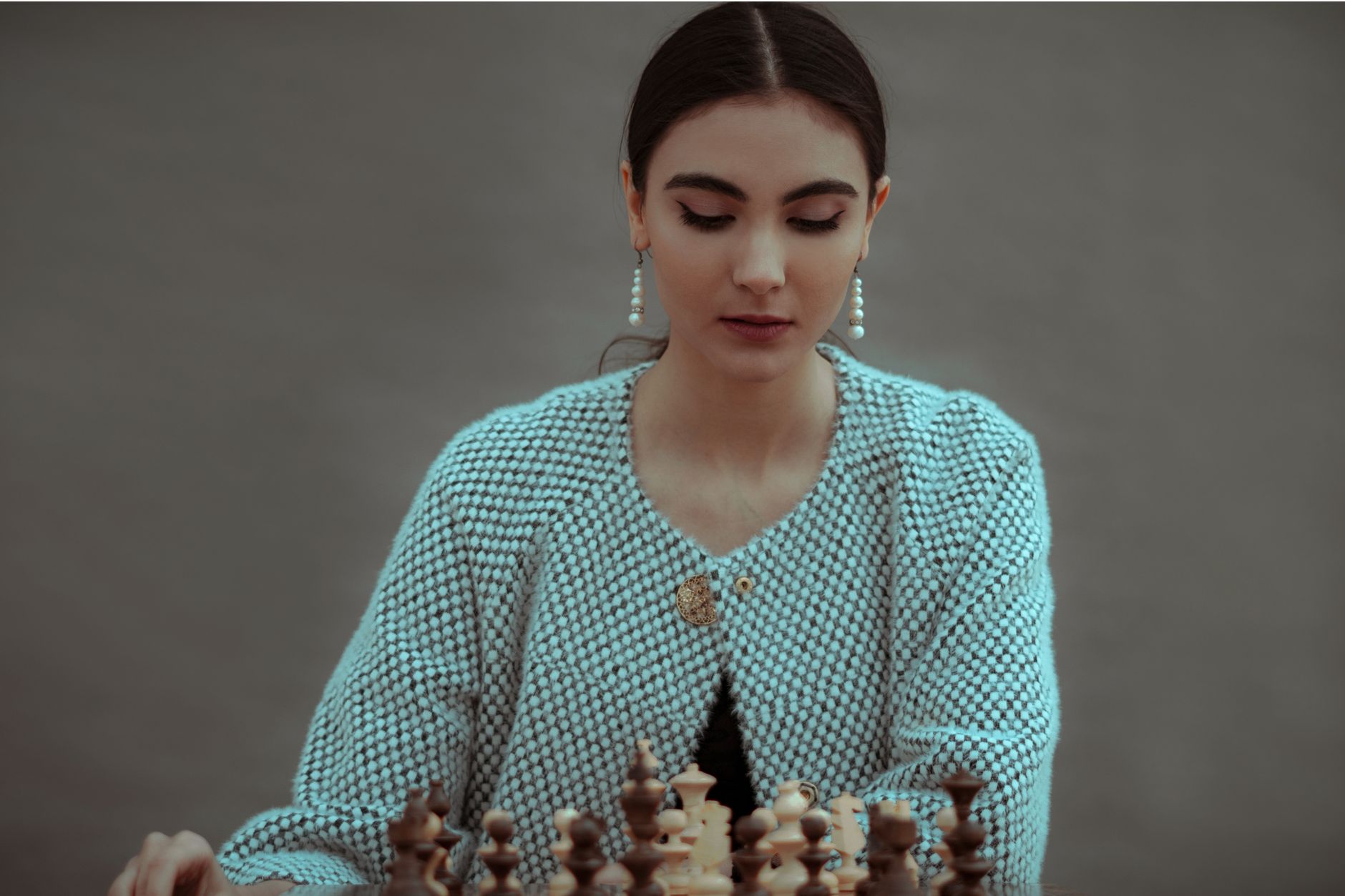 Concentrated ethnic female player sitting at table and playing chess board game of strategic skill against gray background