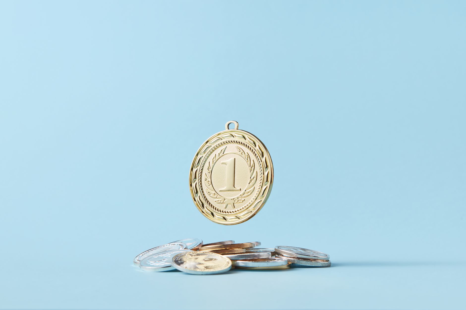 A gold medal and pile of coins on a light blue background representing achievement and savings.