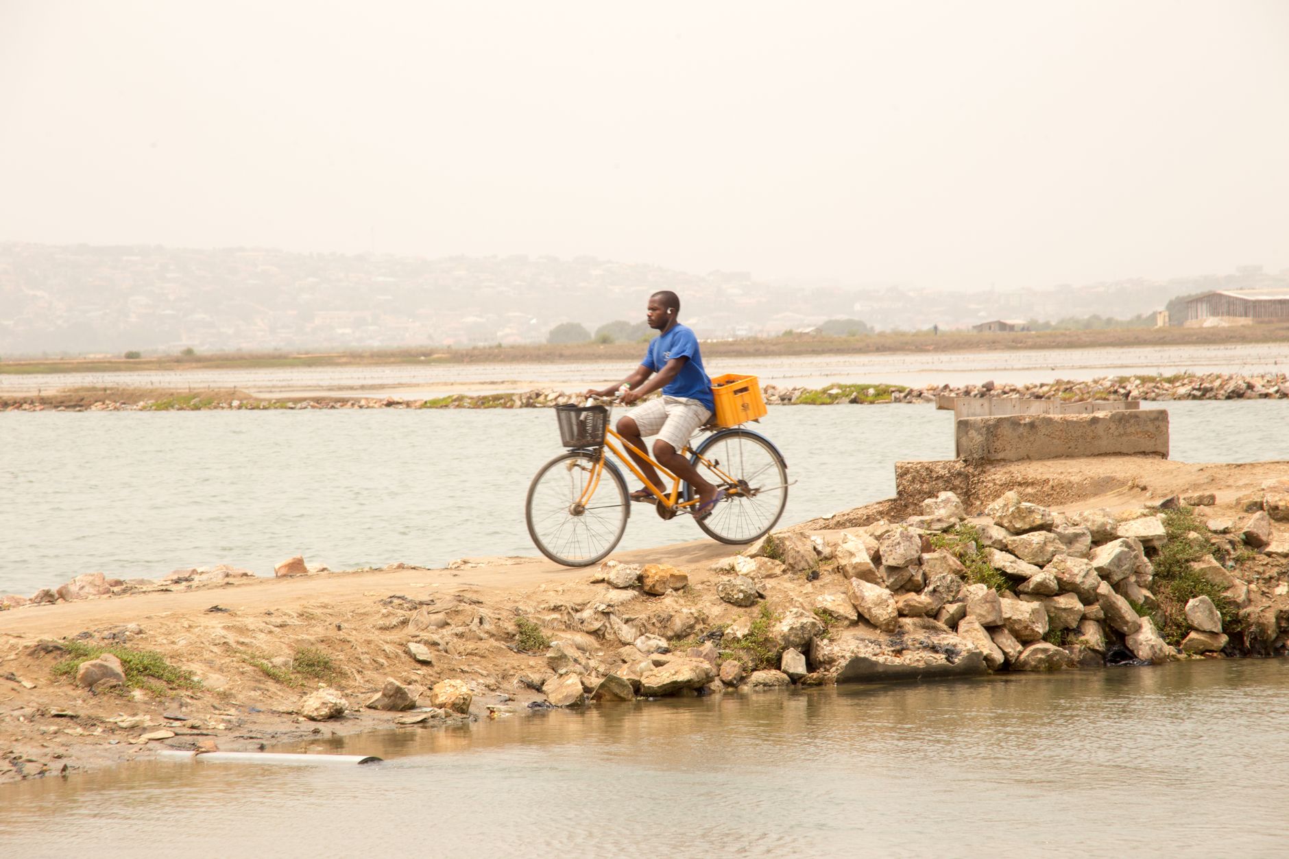 A man cycling by a tranquil lake on a rocky path under a clear sky, enjoying a peaceful ride.