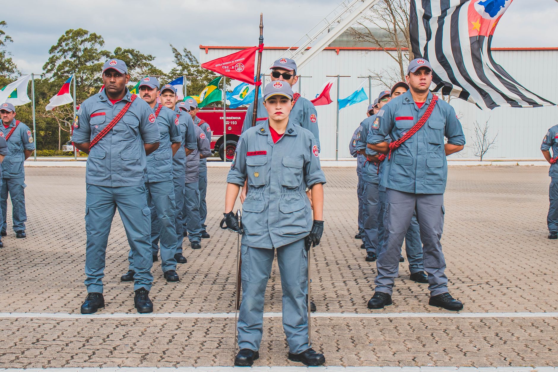 Uniformed soldiers standing in formation outdoors with flags displayed in the background.