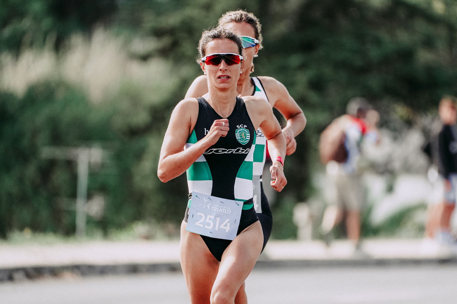 Concentrated slim sportswomen in short tracksuits and dark eyeglasses with hair tied up taking part in competition in summertime