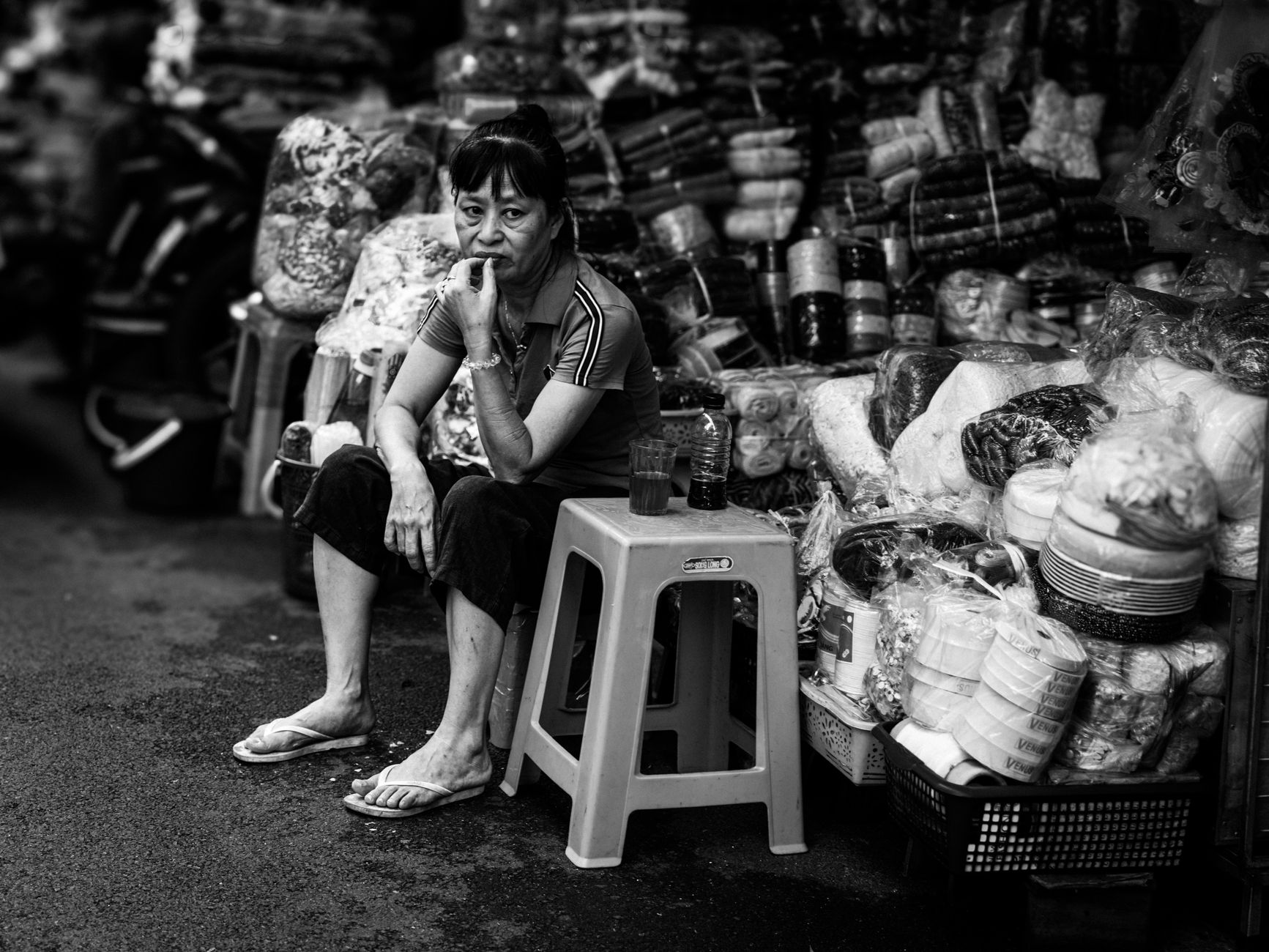 Street vendor sitting among goods in a Hanoi market, Vietnam, showcasing local commerce and lifestyle.