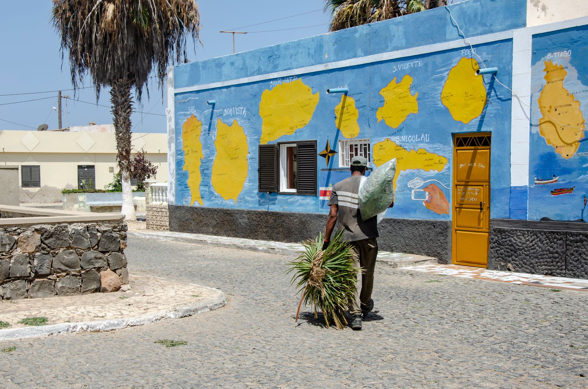 A man walks beside a colorful mural depicting Cape Verde islands on a sunny day.