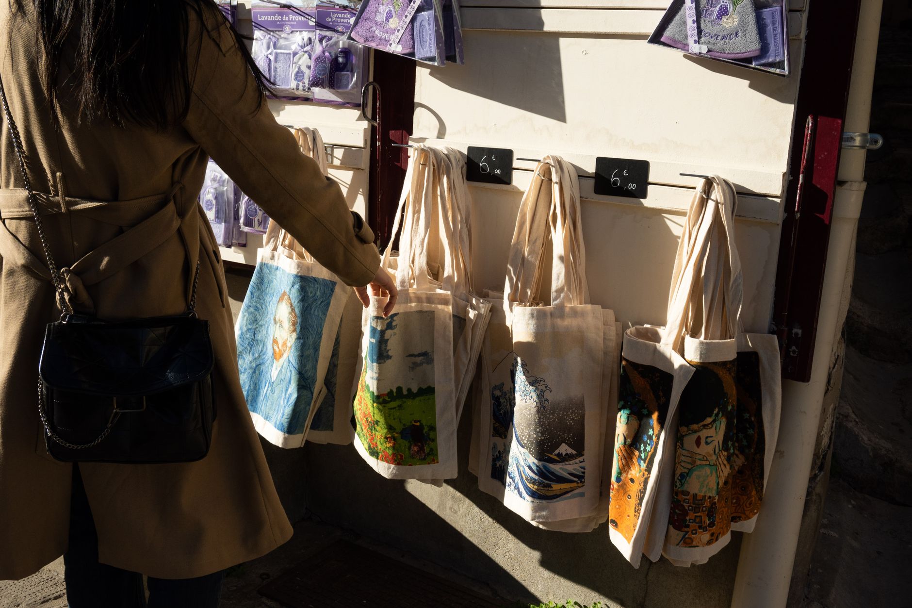 A woman shopping for artistic tote bags at a street market in Arles, France.