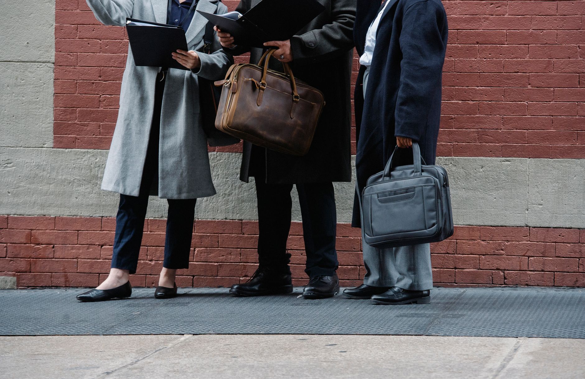 Crop unrecognizable managers in stylish formal outfits standing on city street with document folders and briefcases in hands and discussing new business plans