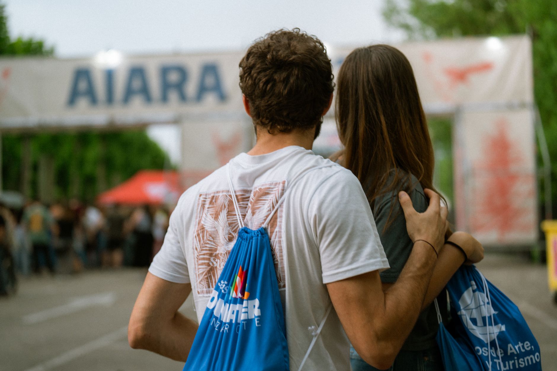 Couple embracing at the entrance of an outdoor event amid a bustling crowd.