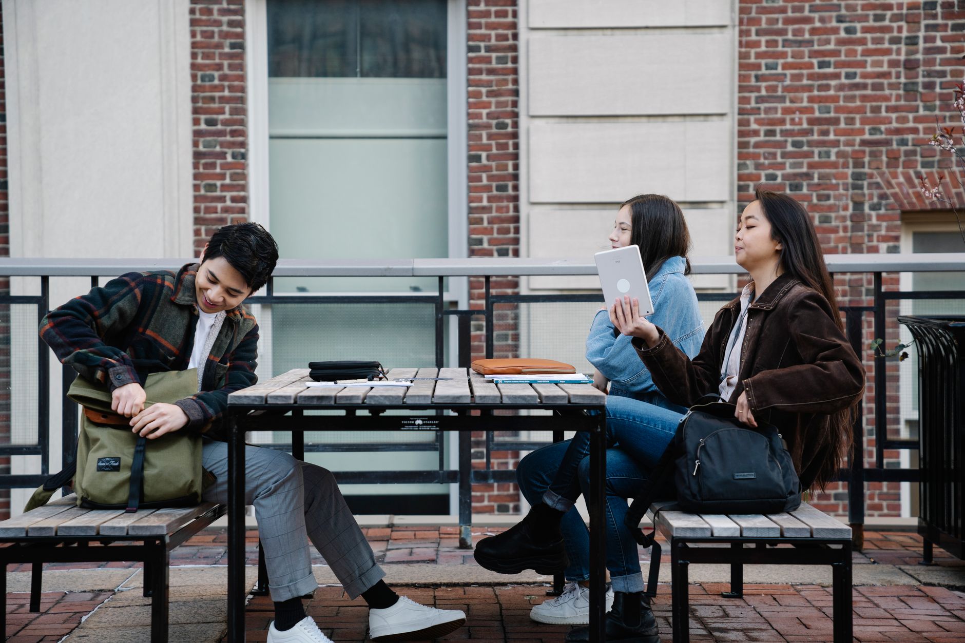 Three college students enjoy a study break on an outdoor patio, engaging with each other.