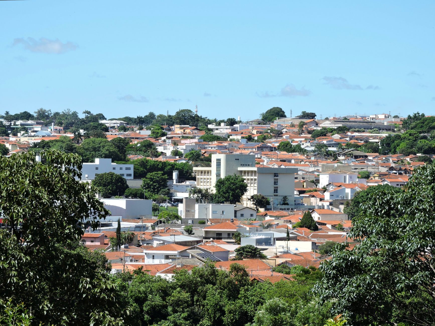Aerial view of Itapira, São Paulo, with prominent red-tiled roofs and lush greenery under clear blue skies.