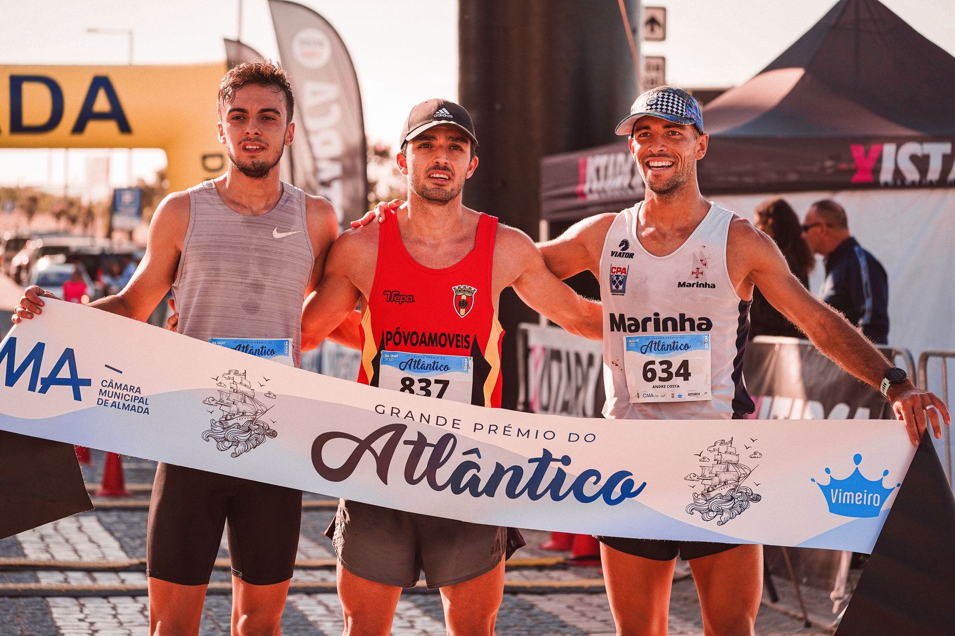 Three marathon runners celebrate their victory at the Grande Prémio do Atlântico in bright outdoor conditions.