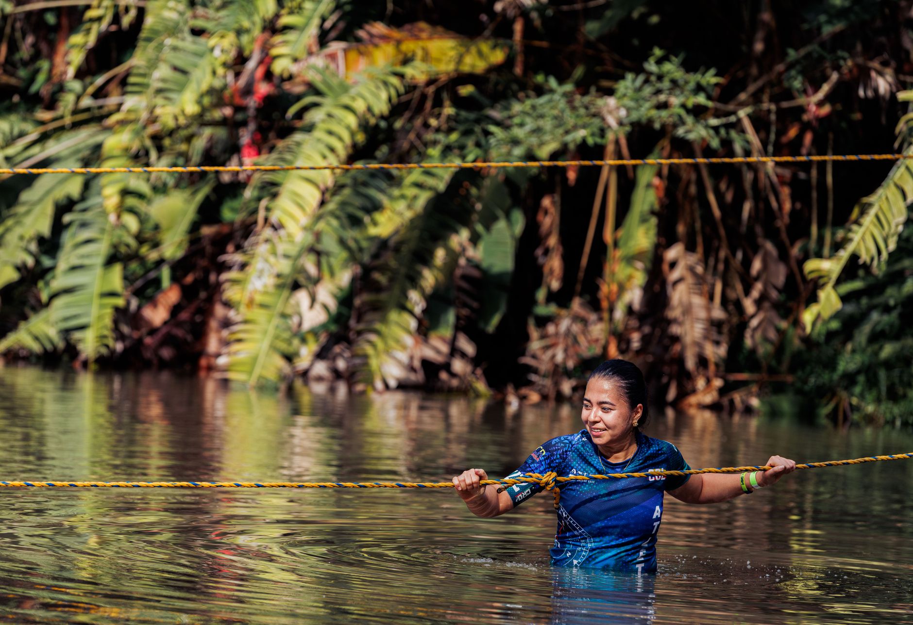 A woman enjoys an outdoor adventure crossing a river in the lush jungle of Risaralda, Colombia.