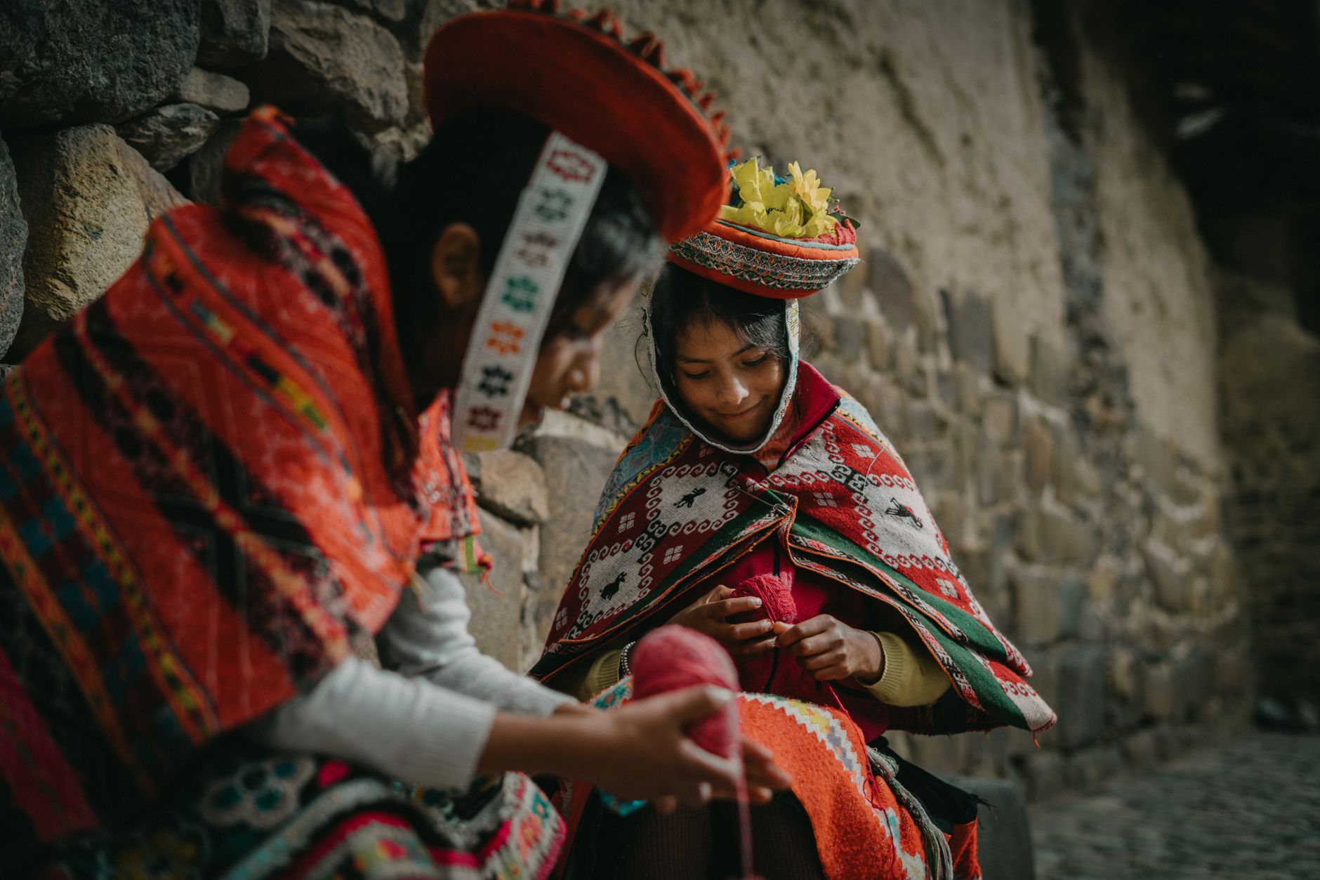 Peruvian women weaving in traditional attire, showcasing vibrant cultural heritage in Ollantaytambo, Cuzco.