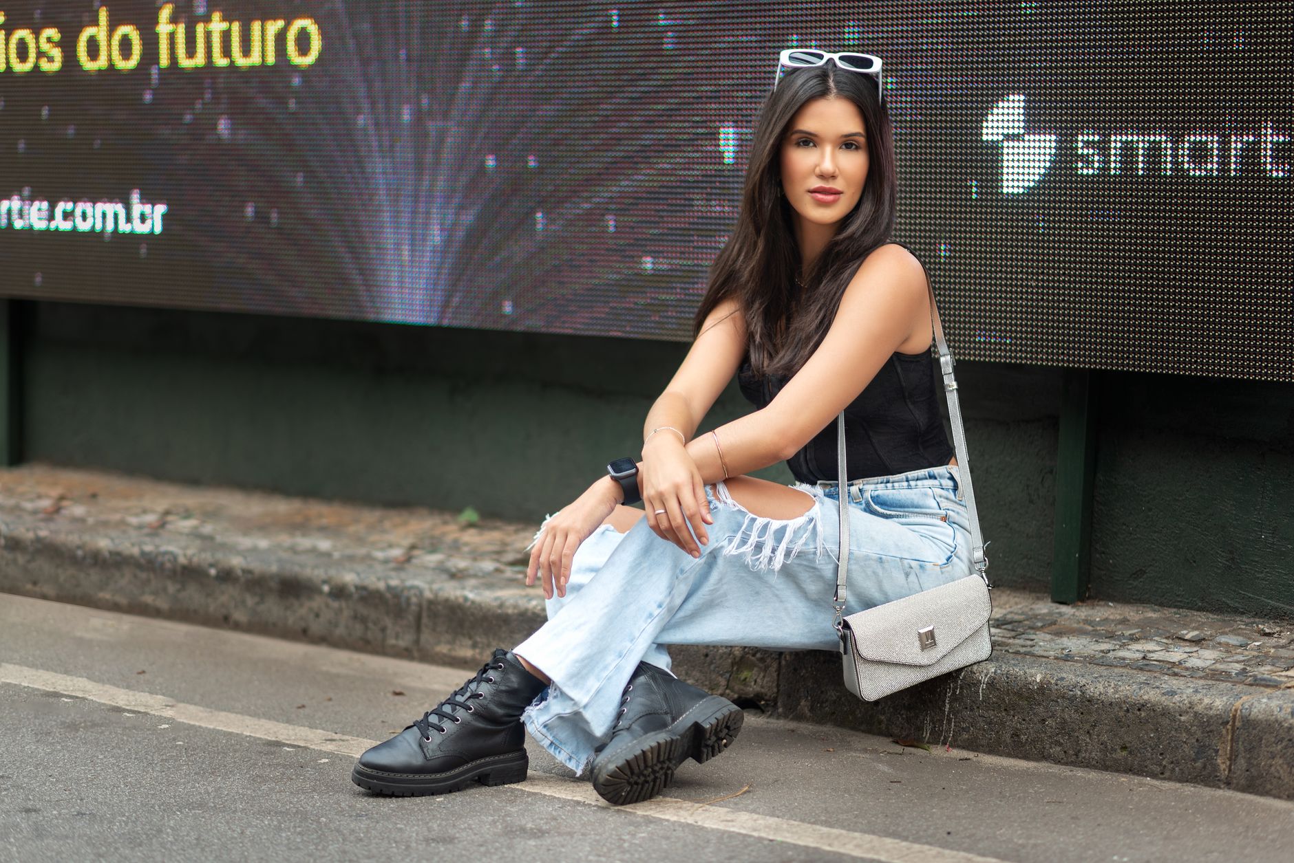 Fashionable woman in casual outfit sitting on a city sidewalk in Nova Lima, Brazil.