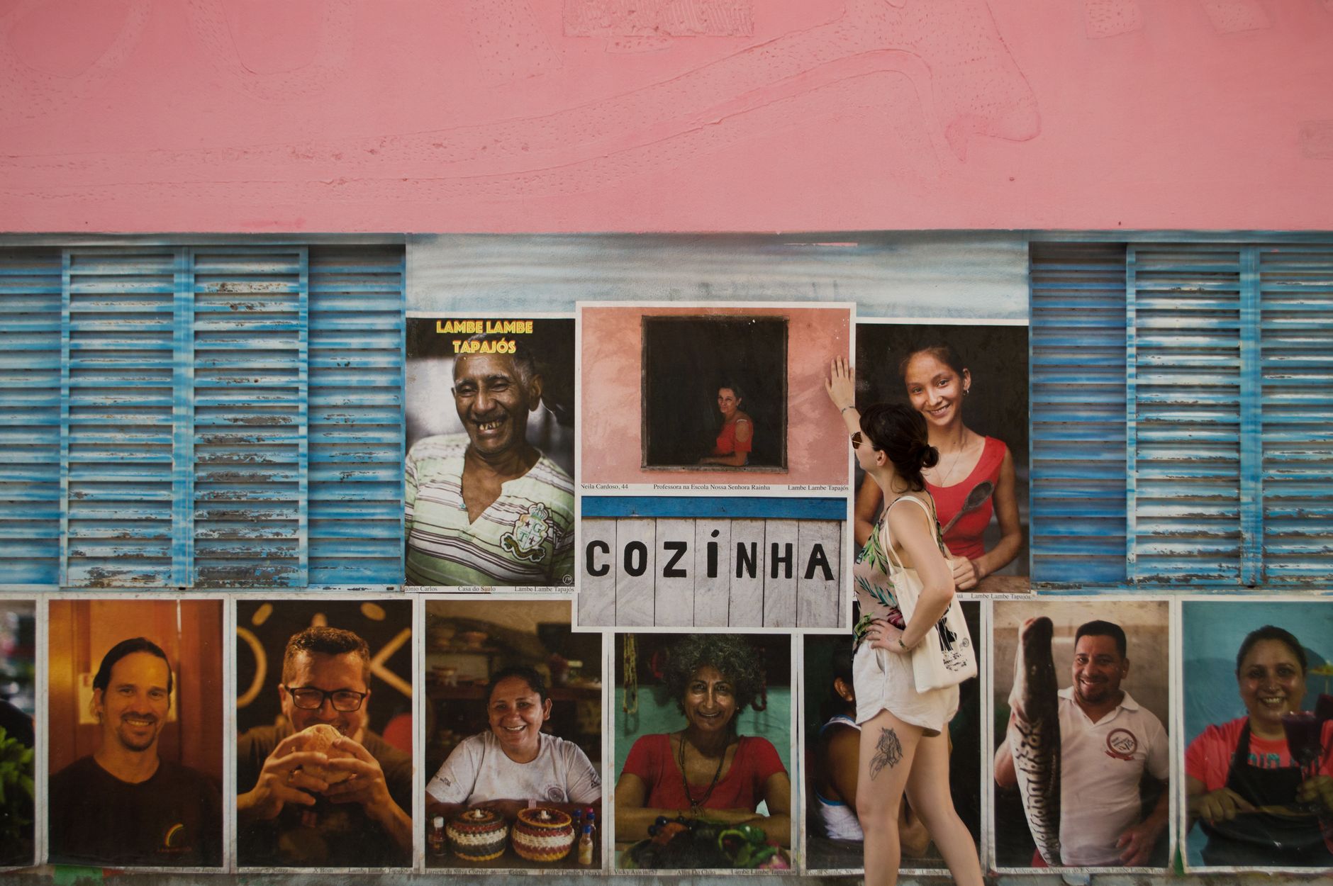 Woman admires vibrant portraits on an urban Brazilian wall.