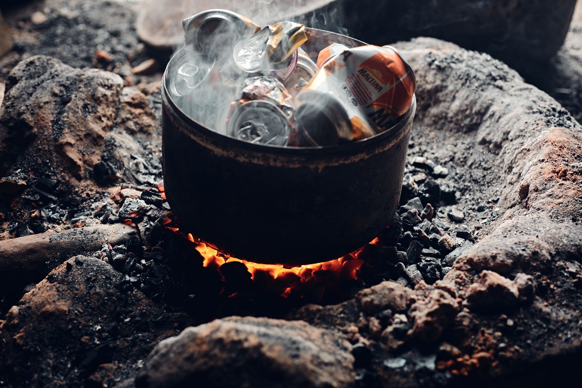 Aluminum cans are melted in a fire pit for recycling. Earthy tones and warm atmosphere.