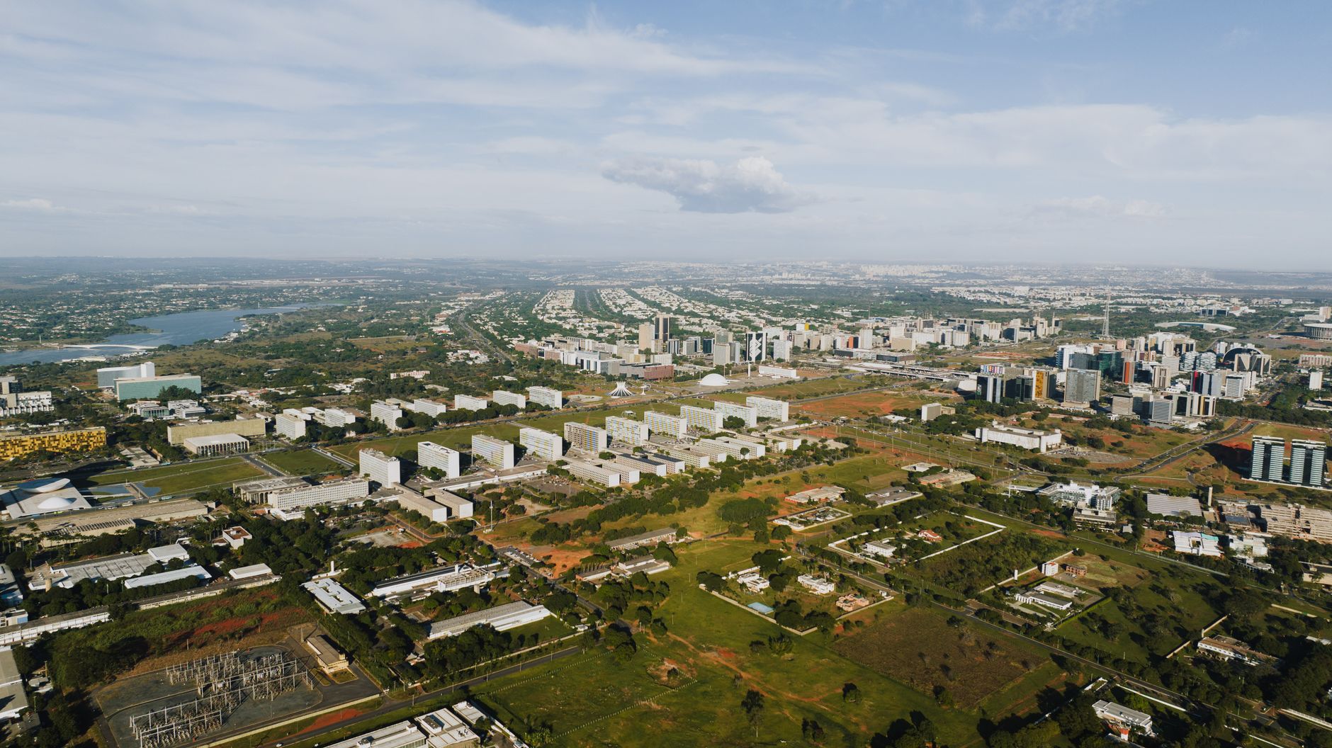 Aerial shot of Brasília showcasing its urban landscape, buildings, and greenery in daylight.
