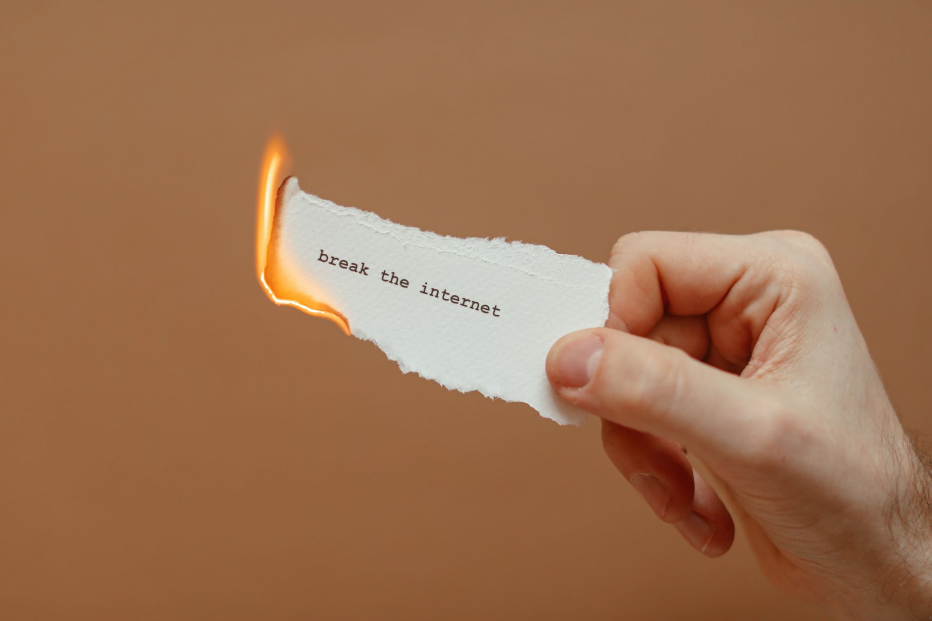 Close-up of a hand holding a burning paper with 'break the internet' text.