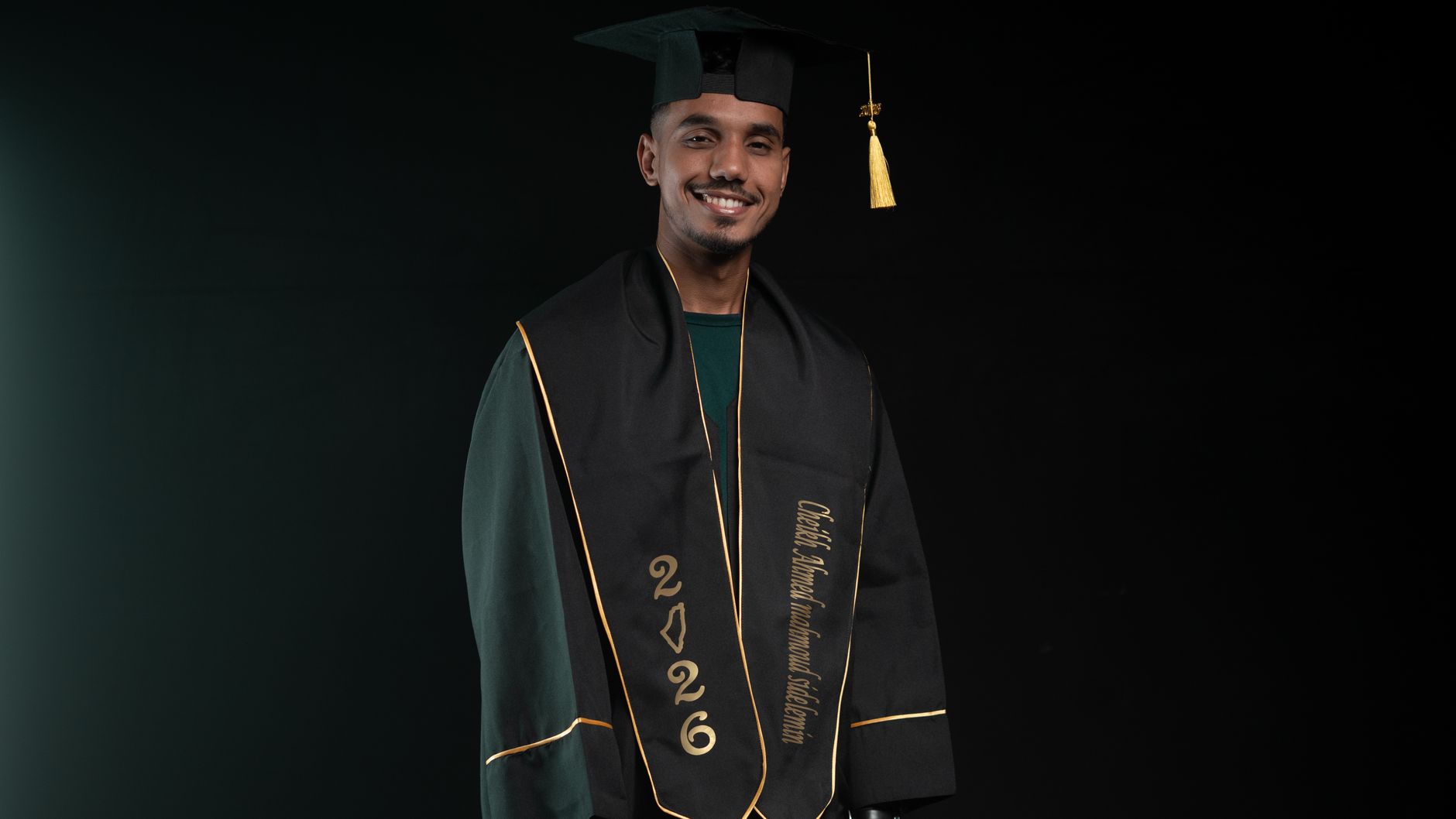 Portrait of a young male graduate smiling in cap and gown with of 2026 inscription.