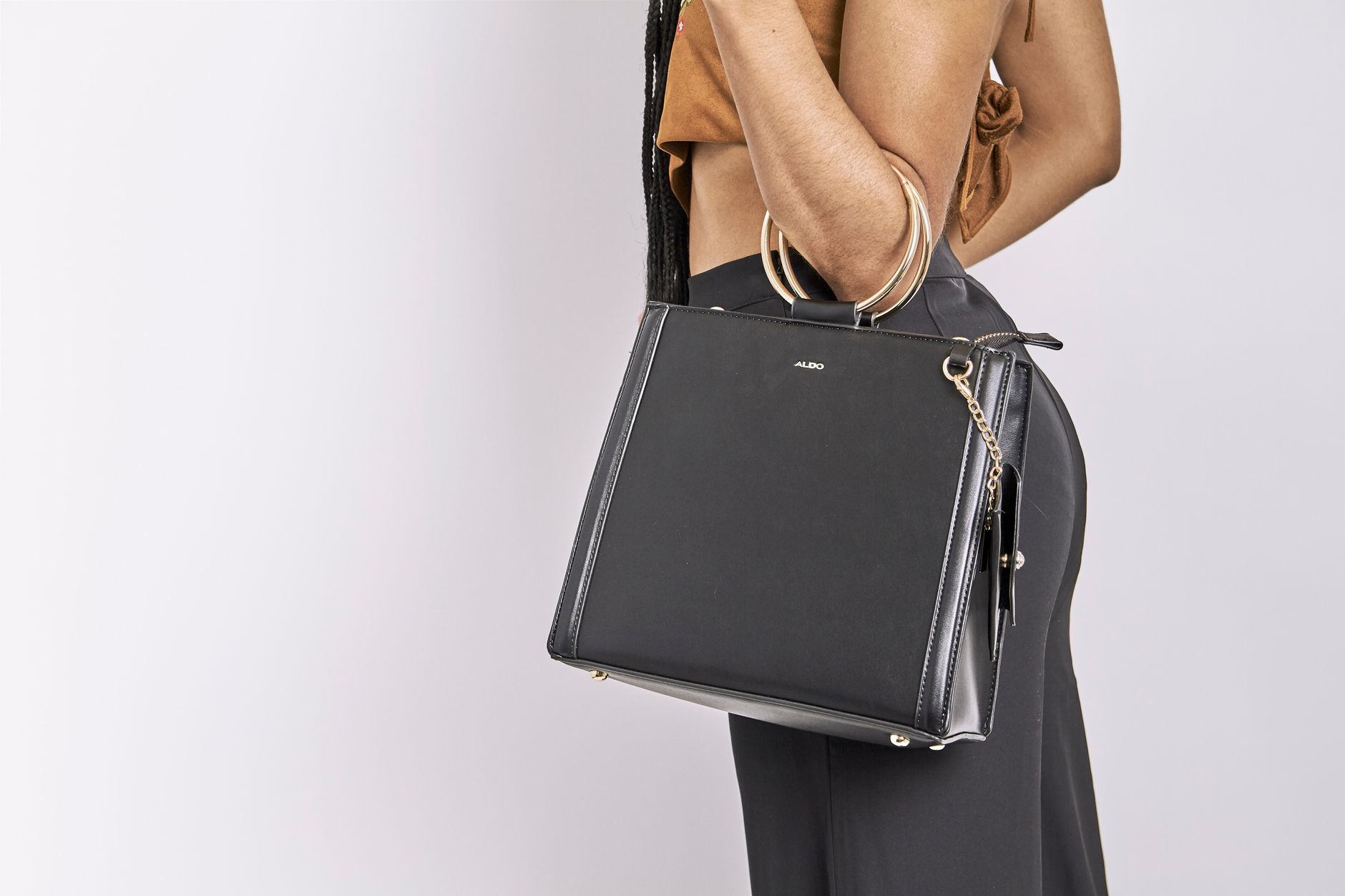 A fashionable woman holding a chic black leather handbag against a white background, showcasing style and elegance.