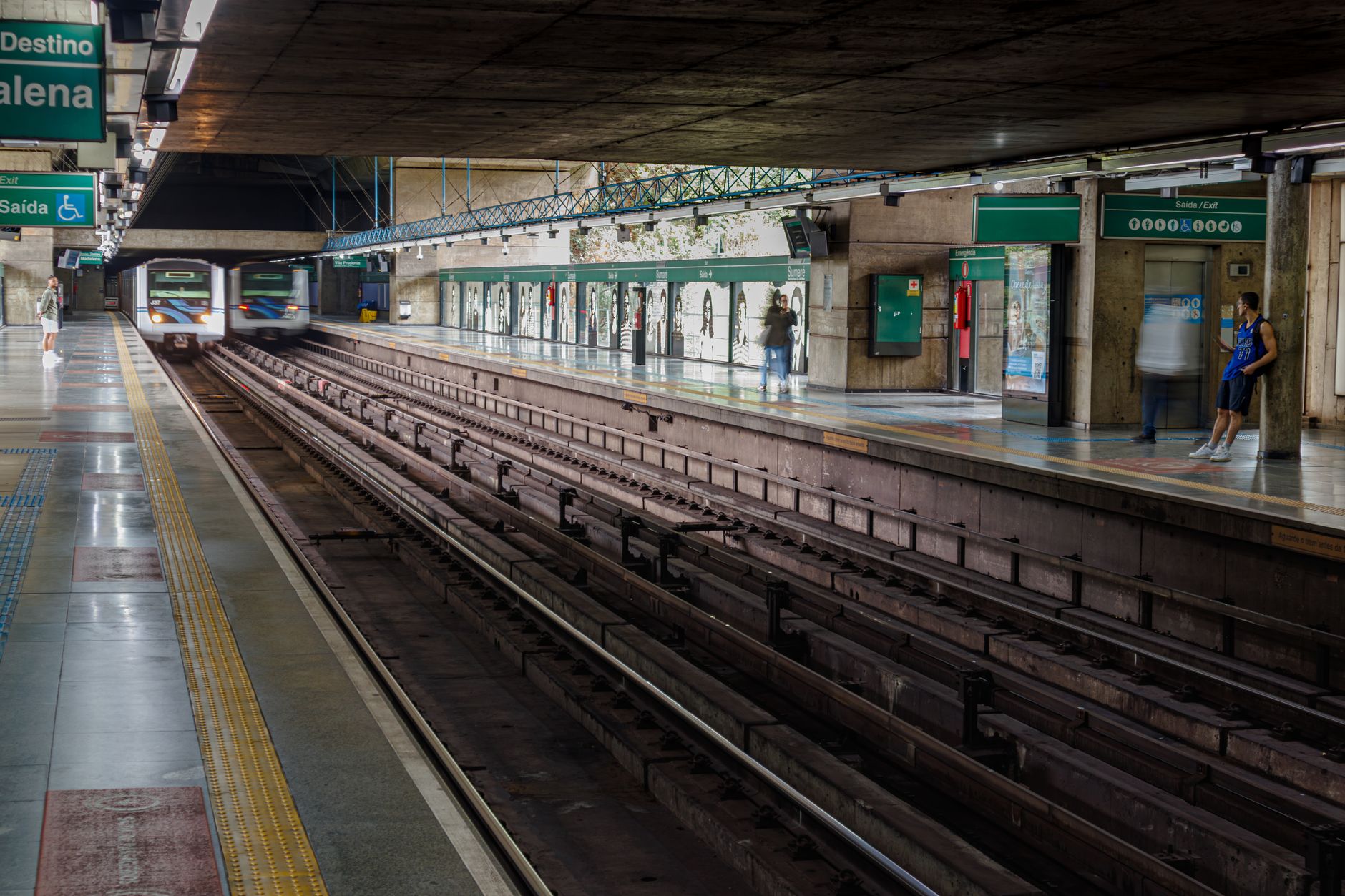 A busy subway station in São Paulo with an incoming train and passengers waiting on the platform.