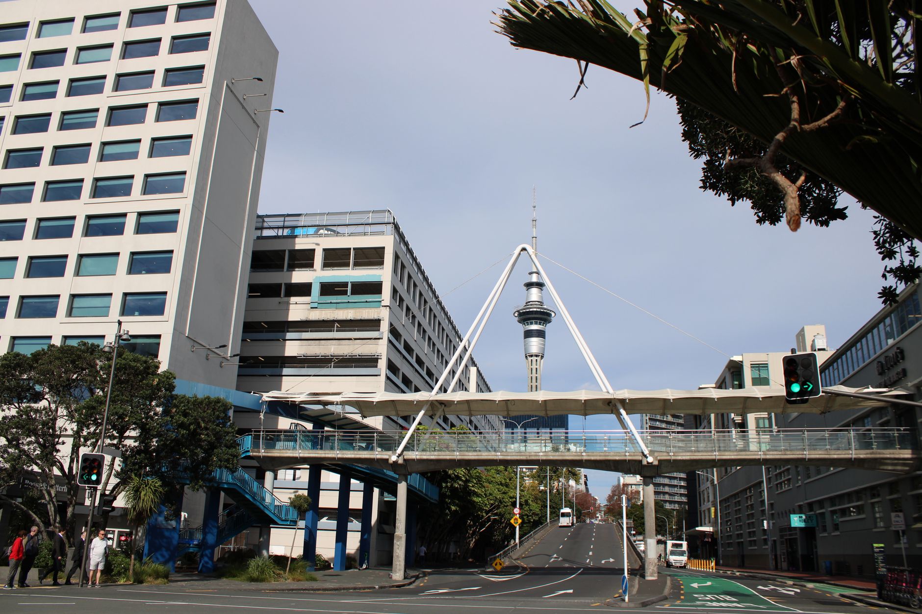 Urban scene featuring a pedestrian bridge and iconic Skytower in a bustling cityscape.