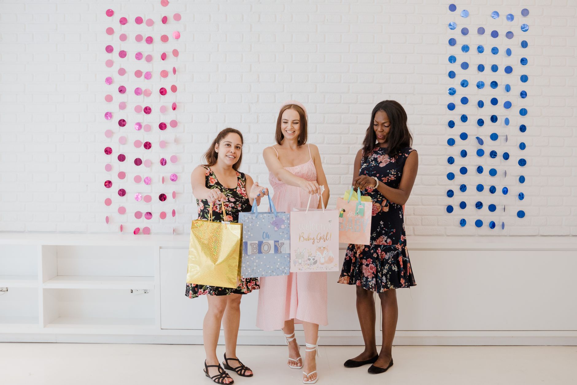 Three women celebrating a baby shower with colorful gift bags and decorations.