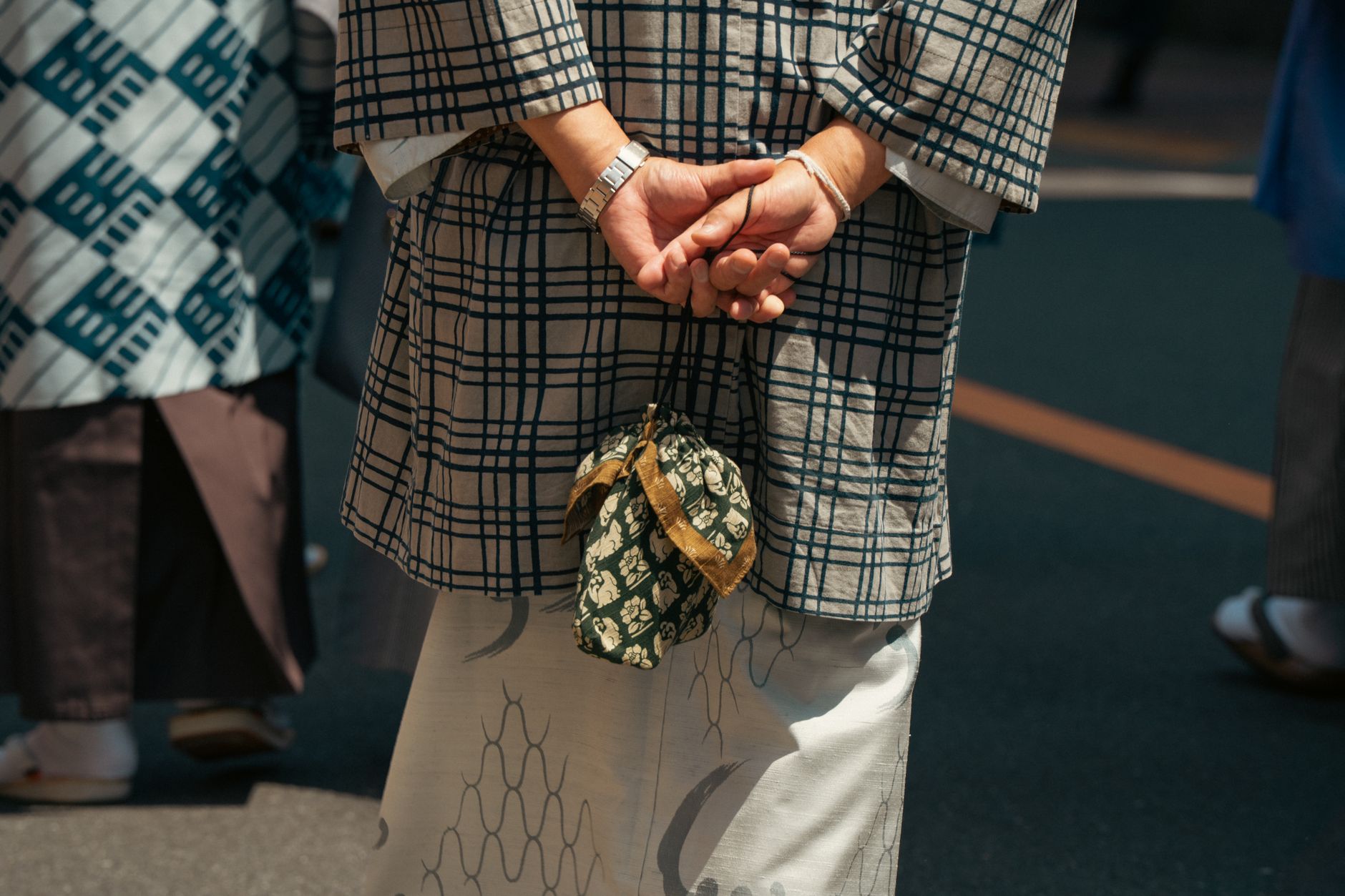 Person in traditional Japanese kimono standing on a Tokyo street, hands clasped behind back.