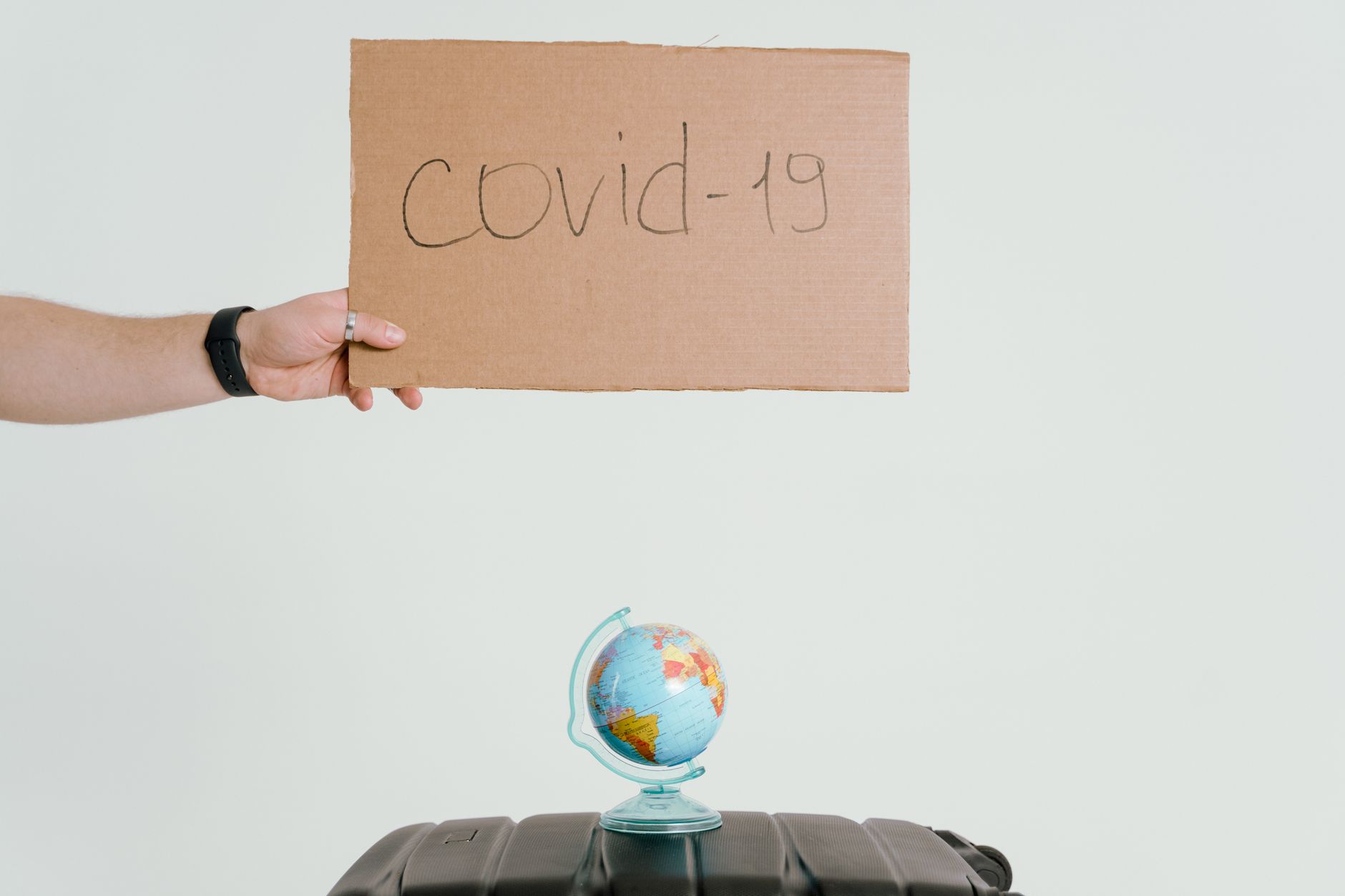 Hand holding covid-19 sign over globe and luggage, symbolizing pandemic travel impact.