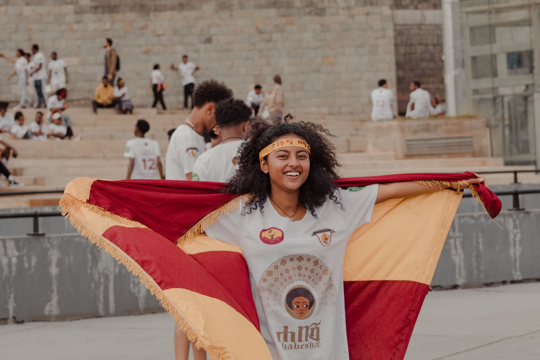 Smiling woman holding a vibrant flag at an outdoor gathering, exuding happiness and cultural pride.