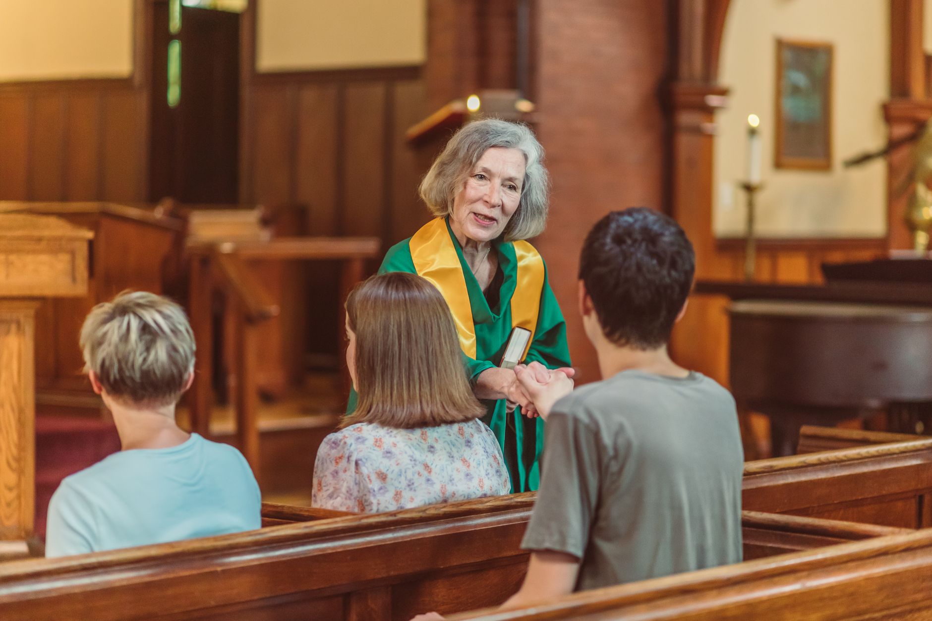 An elderly female clergy in church greets and interacts with congregants during a service.
