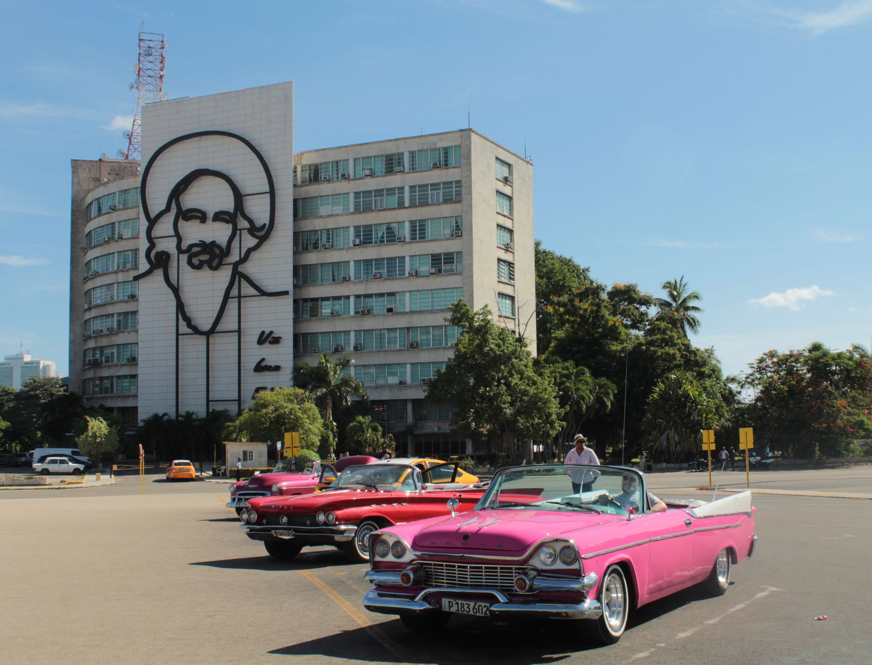 Classic American cars parked by iconic Cuban landmark in sunny Havana street.