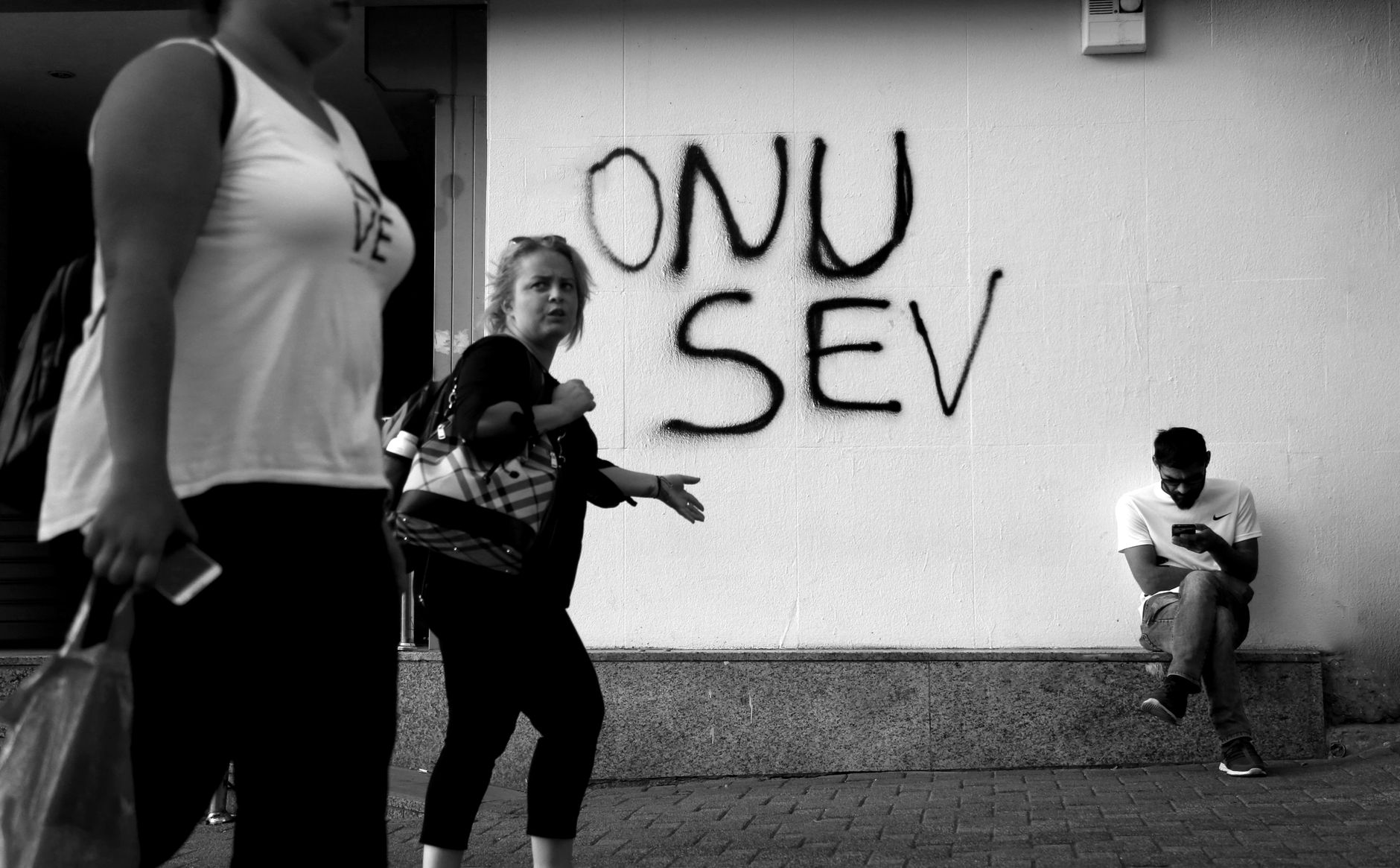 Black and white street photo showcasing graffiti text and passersby, capturing urban life.