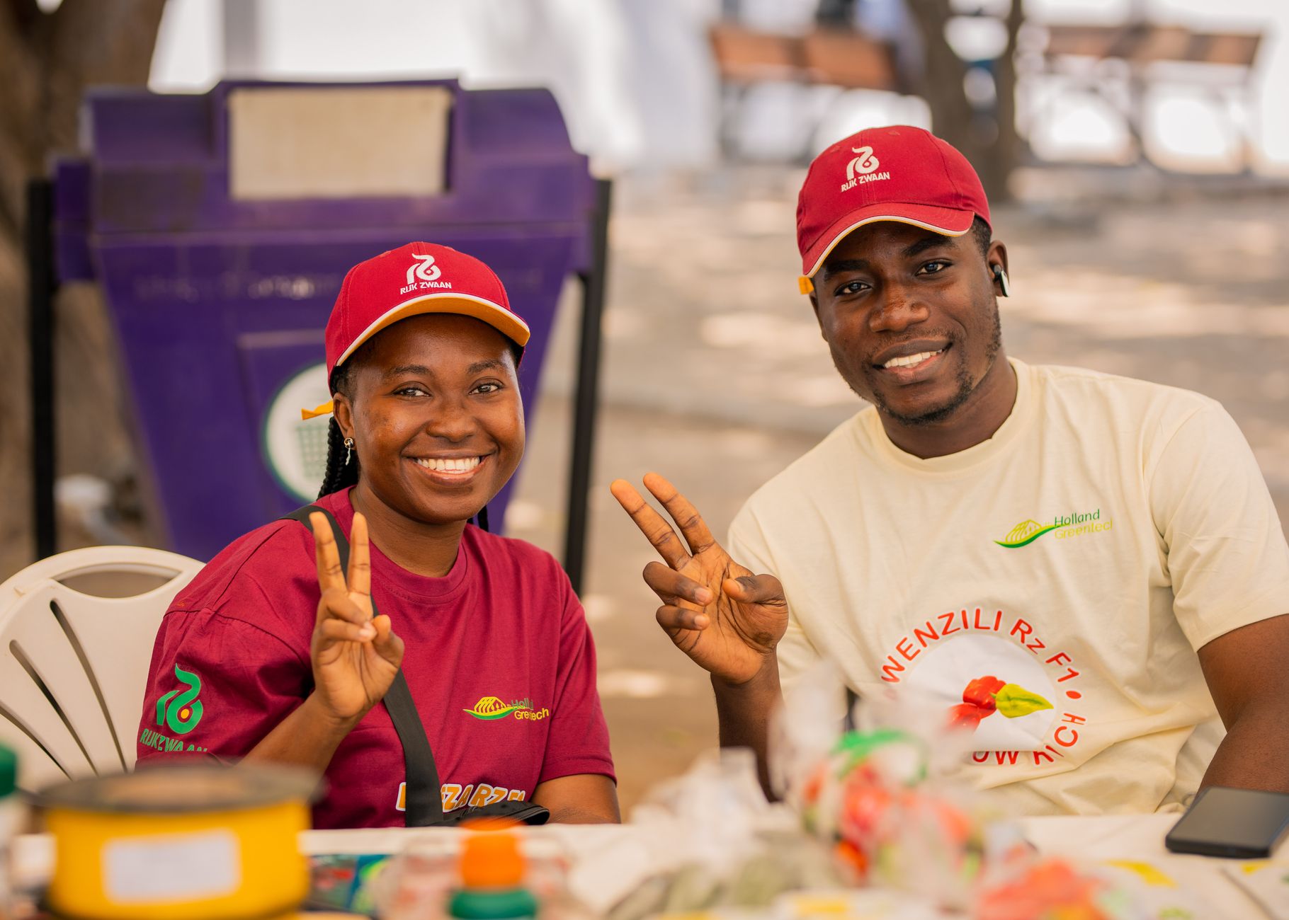Two market vendors smiling and posing with peace signs. Bright and lively outdoor setting.