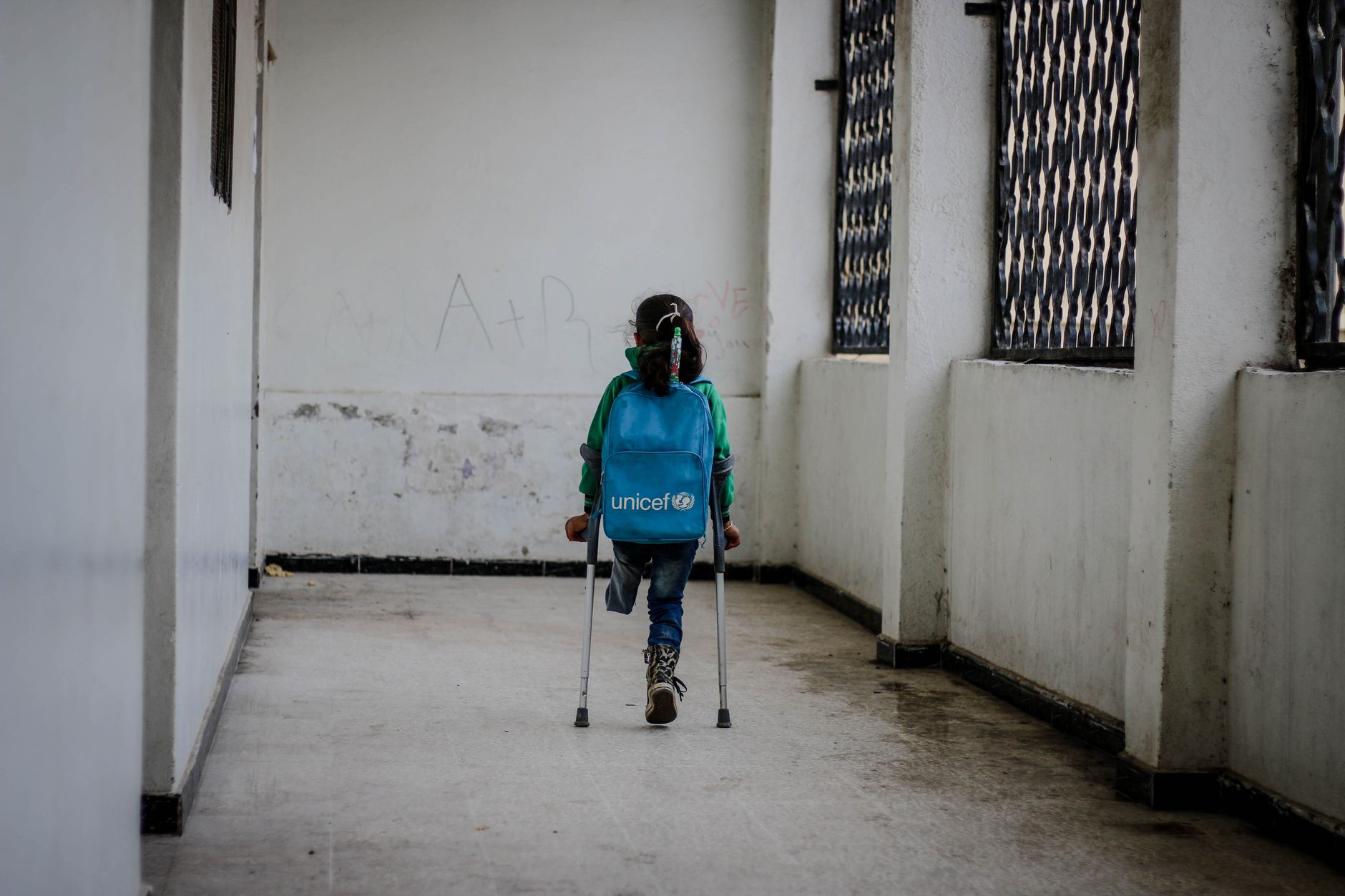 Back view of anonymous girl with crutches and leg amputation in shabby building in daytime